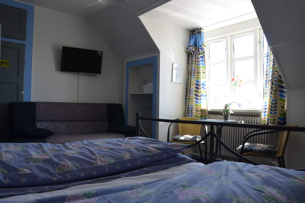 A bedroom with two beds, a television on the wall, a window with curtains, and a radiator.