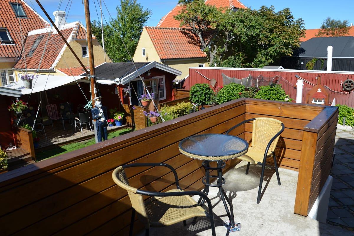 A wooden deck with a table and chairs, surrounded by a red fence and greenery.