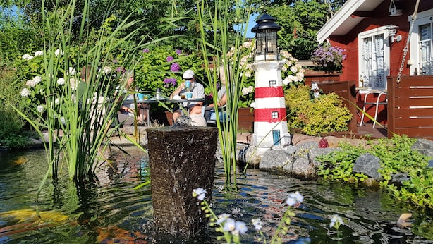 Een rustige tuin met een vijver, een vuurtoren en een houten constructie.