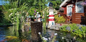 A serene garden with a pond, a lighthouse, and a wooden structure. - Ferie På Toppen (Skagen)