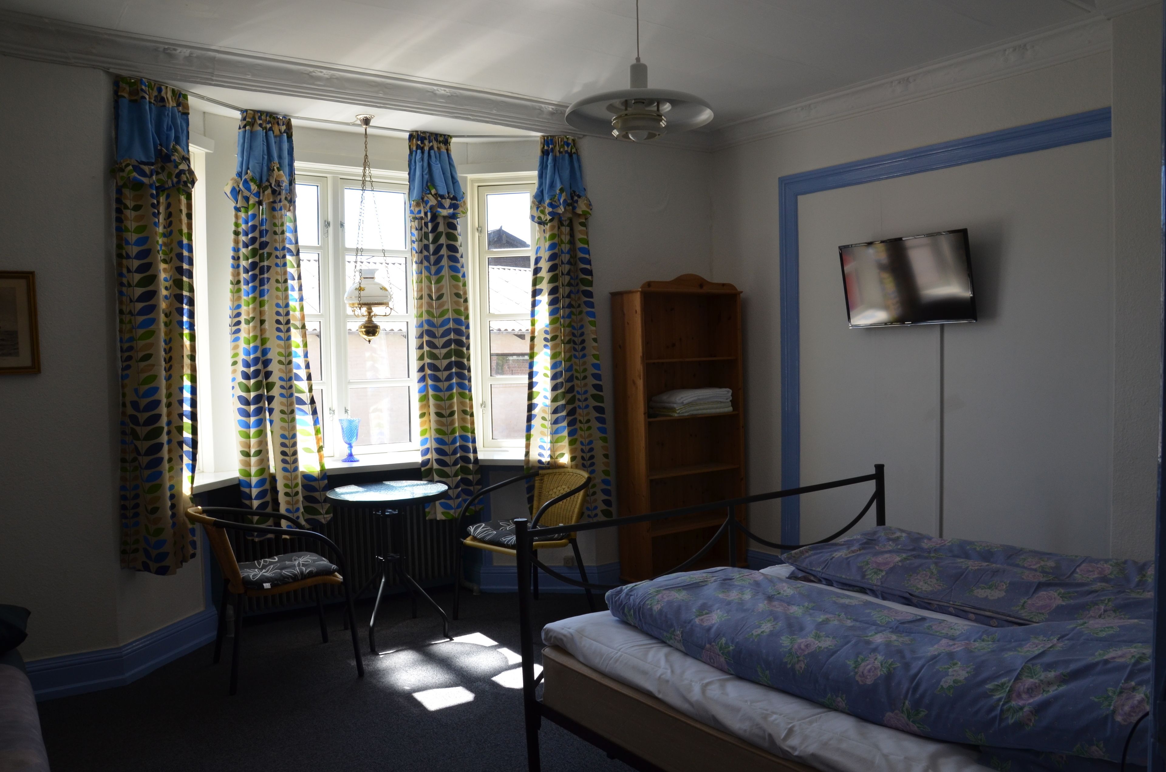 Ein Schlafzimmer mit einem Bett, einem Sessel, einem kleinen Tisch, einem Bücherregal und einem an der Wand befestigten Fernseher.
