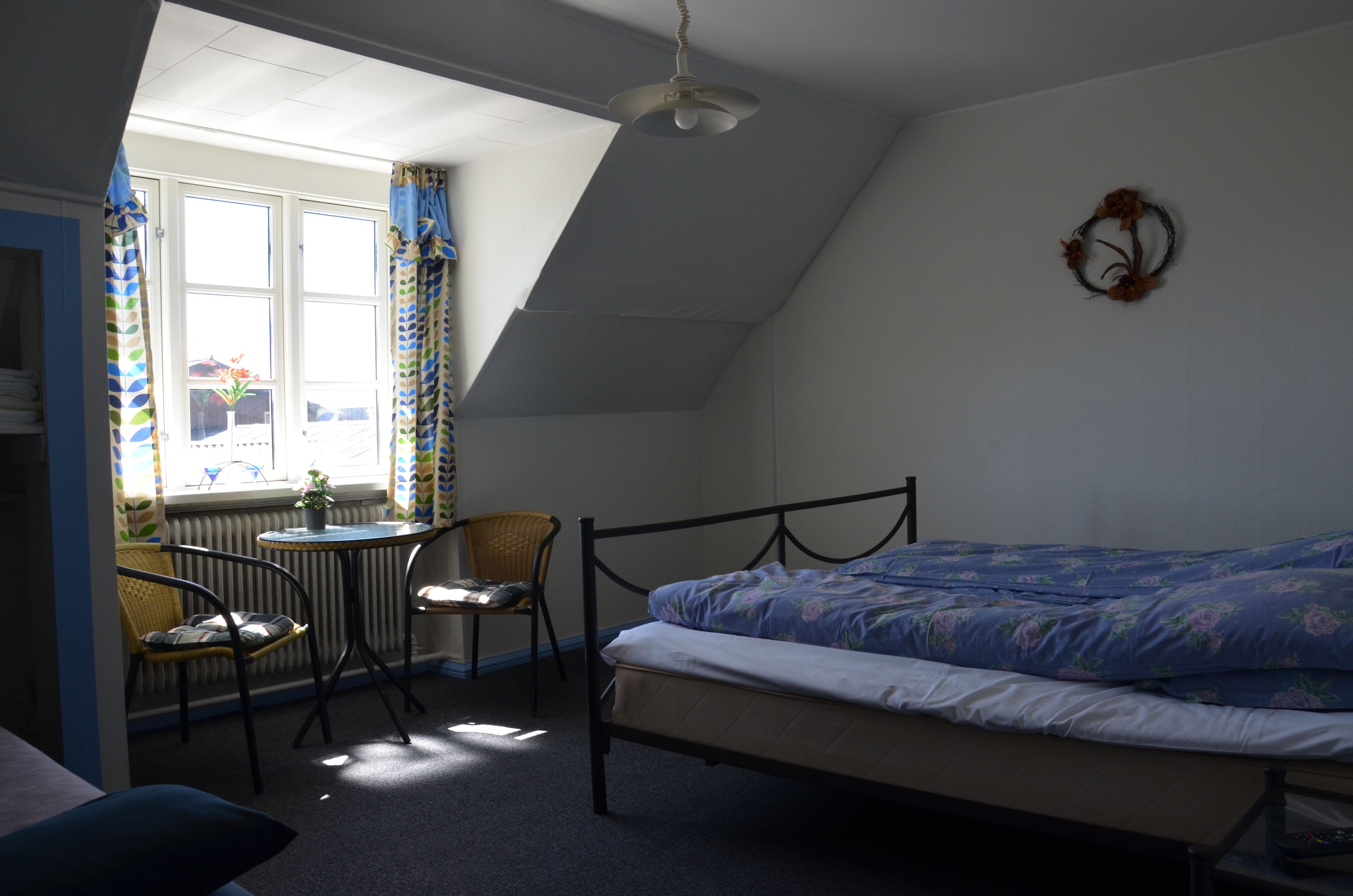 Une chambre à coucher avec un lit, une chaise, une table et une fenêtre avec des rideaux.