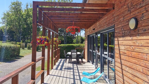 A wooden deck with a pergola, outdoor seating, and hanging flower baskets. - Camping La Tourelle (Plémy)