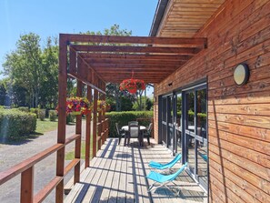 Una terraza de madera con pérgola, mobiliario exterior y cestas colgantes de flores.