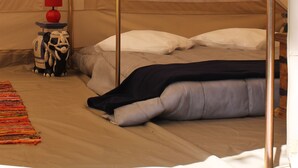 A tent with a bed, a red lamp, and a small table with a red object on it. - Camping La Tourelle (Plémy)