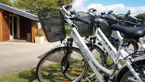 A row of bicycles parked outside a building with a wooden exterior and a metal fence. - Camping La Tourelle (Plémy)
