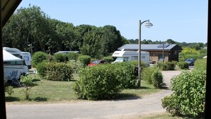 A view from inside a covered area at a campsite, including a gravel path, parked RVs, and a building with a sloped roof. - Camping La Tourelle (Plémy)
