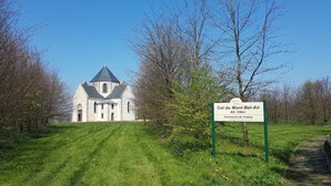 A church with a pointed steeple, surrounded by a grassy area and trees. A sign indicates the name 'Col du Mont Bel-Air' and altitude 'Alt. 336m'. - Camping La Tourelle (Plémy)