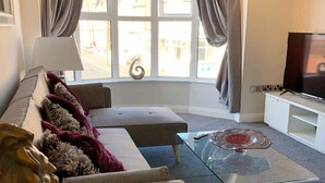 A living room with a sofa, a glass coffee table, a TV, and a window with curtains. - The Place Blackpool (Blackpool)