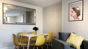 A dining area with a white table, yellow chairs, a mirror, and a grey sofa with a yellow pillow. - The Place Blackpool (Blackpool)
