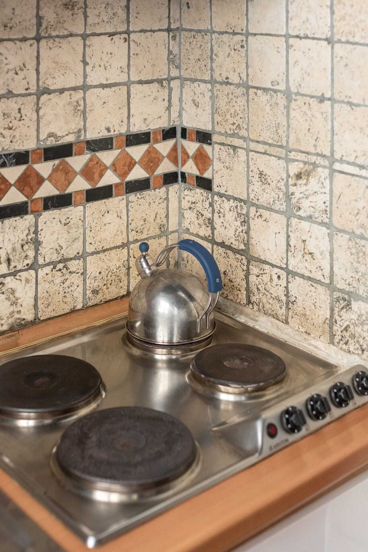 Eine Küche mit Herd, Wasserkocher und gefliestem Spritzschutz.