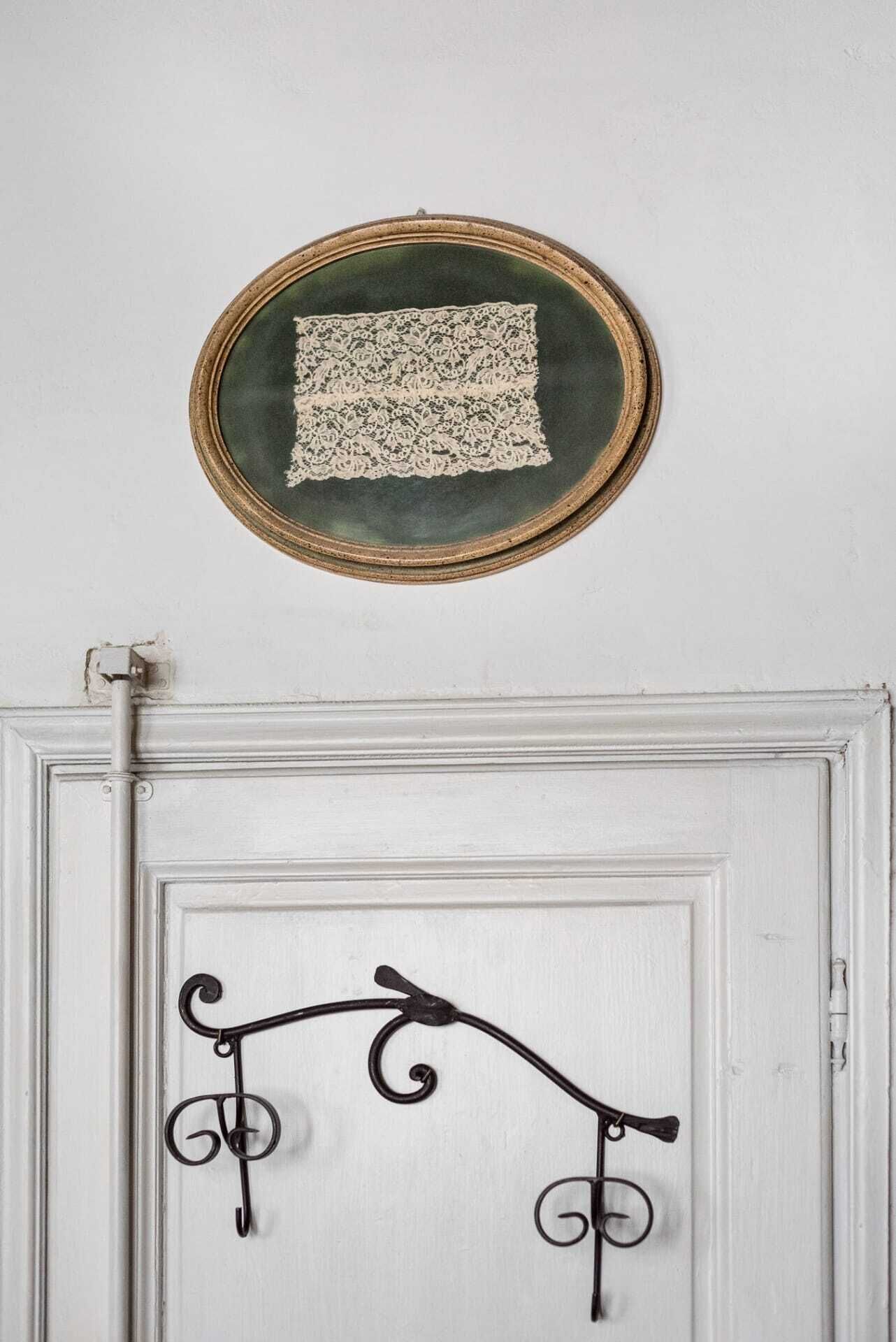 Una puerta blanca con un gancho metálico decorativo y un encaje enmarcado colgando en la pared de arriba.