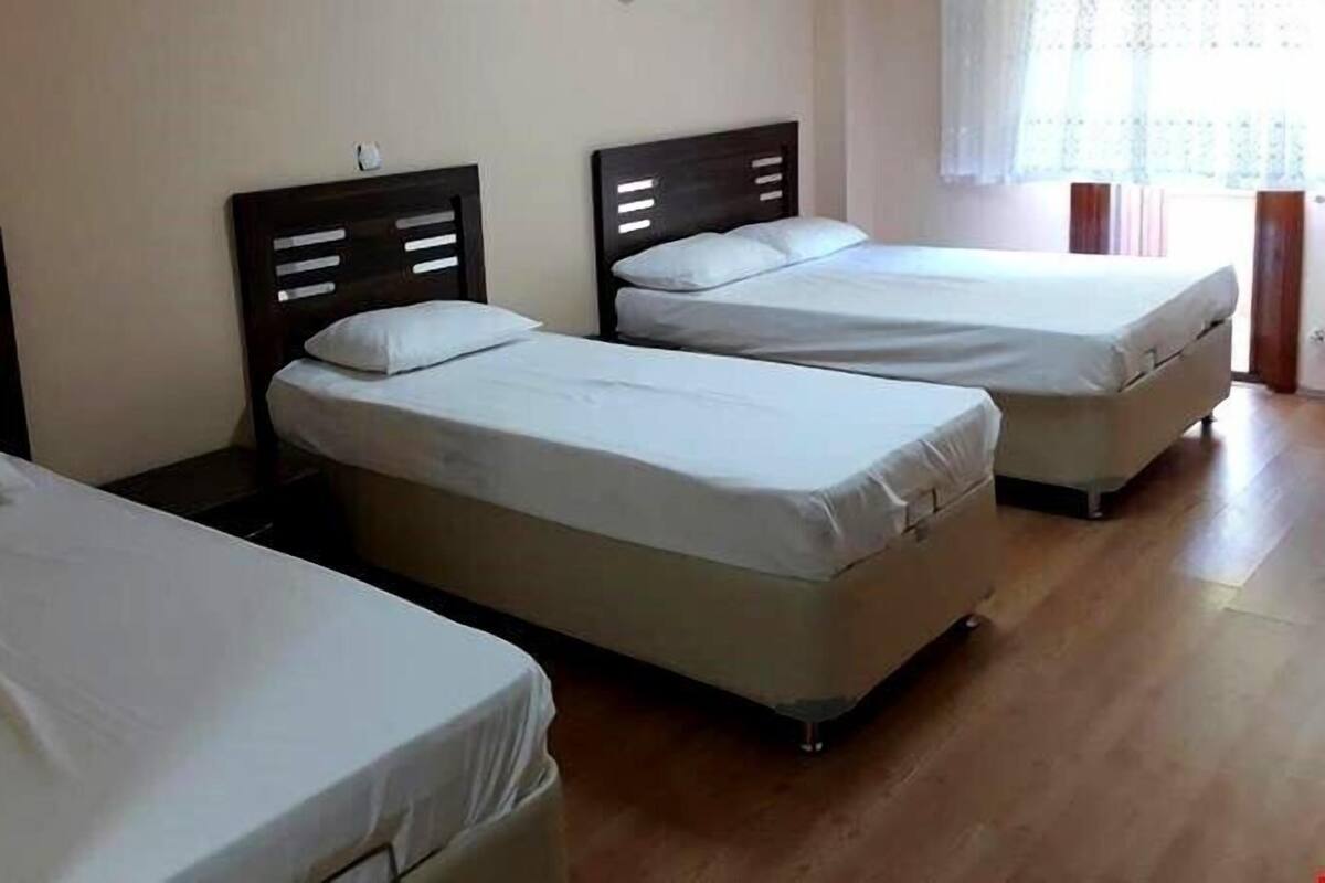 Una habitación con tres camas individuales, cada una con cabecero de madera y ropa de cama blanca.