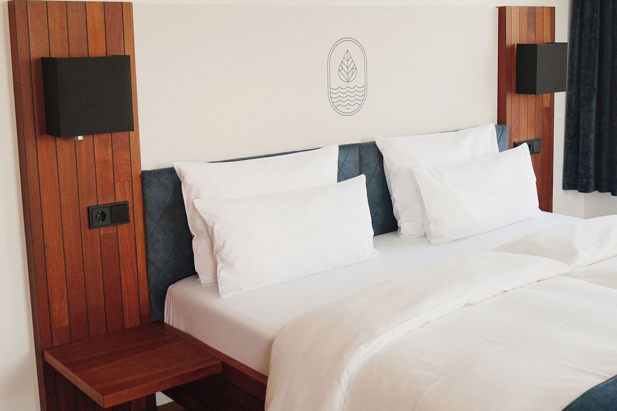 A hotel room with a bed, wooden headboard, two bedside tables, a wall-mounted TV, and a small decorative item.