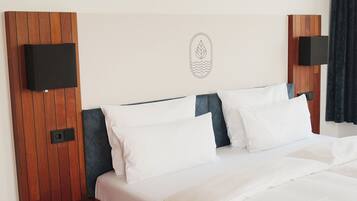 A hotel room with a bed, wooden headboard, two bedside tables, a wall-mounted TV, and a small decorative item.