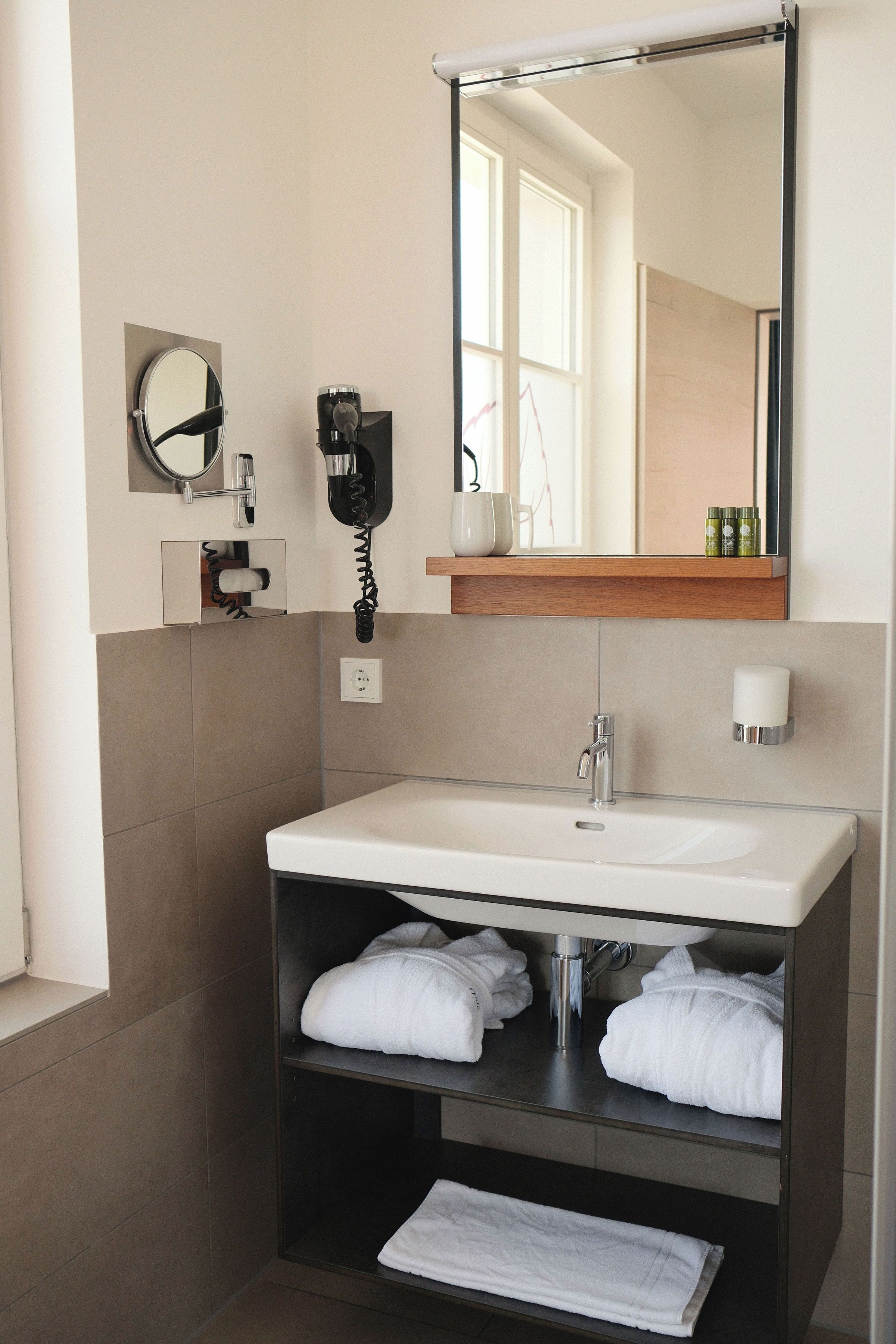 A modern bathroom with a white sink, a mirror, a hairdryer, and a towel rack.