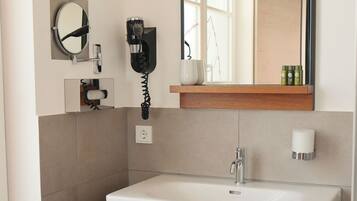 A modern bathroom with a white sink, a mirror, a hairdryer, and a towel rack.