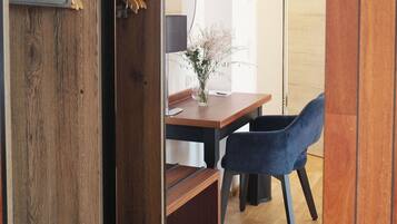 Un armario de madera con perchas, un escritorio con una lámpara, una silla y un jarrón con flores.