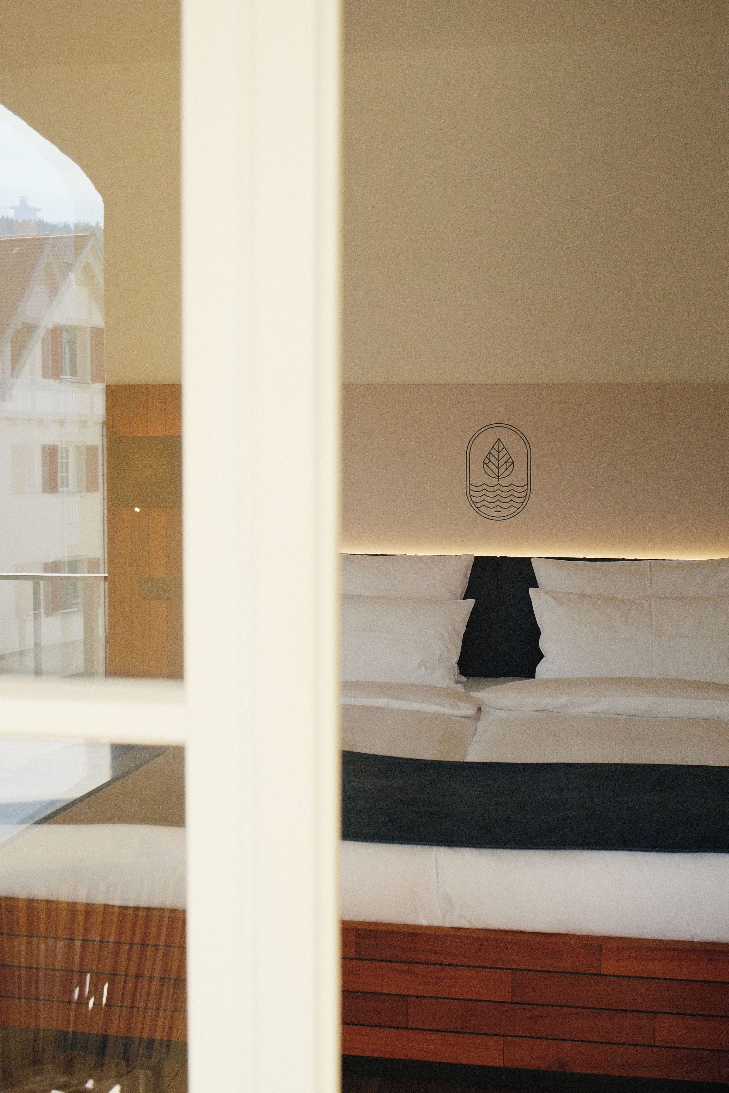 A bedroom with a bed, a wooden headboard, a wall-mounted emblem, and a window view.