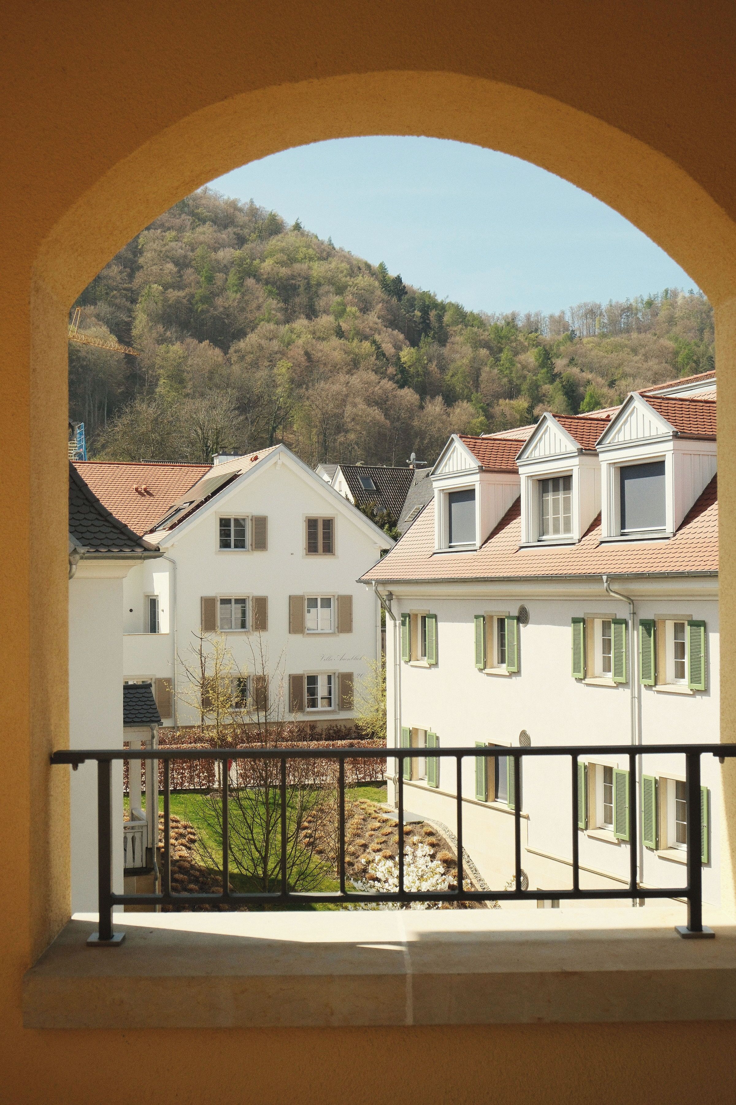 Ein Gebäude mit Balkon und Blick auf einen bewaldeten Hügel, strahlend blauer Himmel.