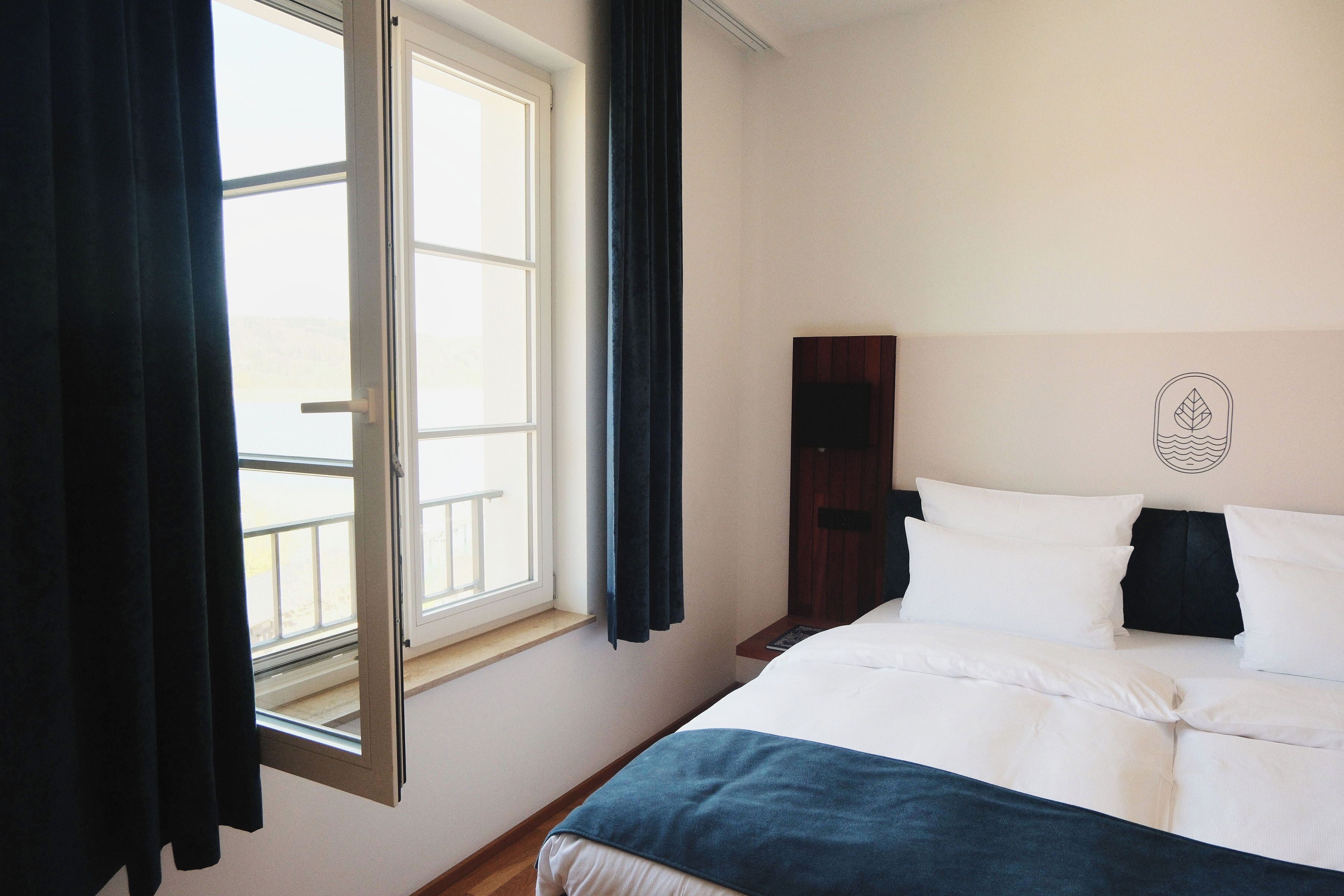 Ein Hotelzimmer mit Bett, einem Fenster mit Vorhängen und einem an der Wand hängenden Kunstwerk.
