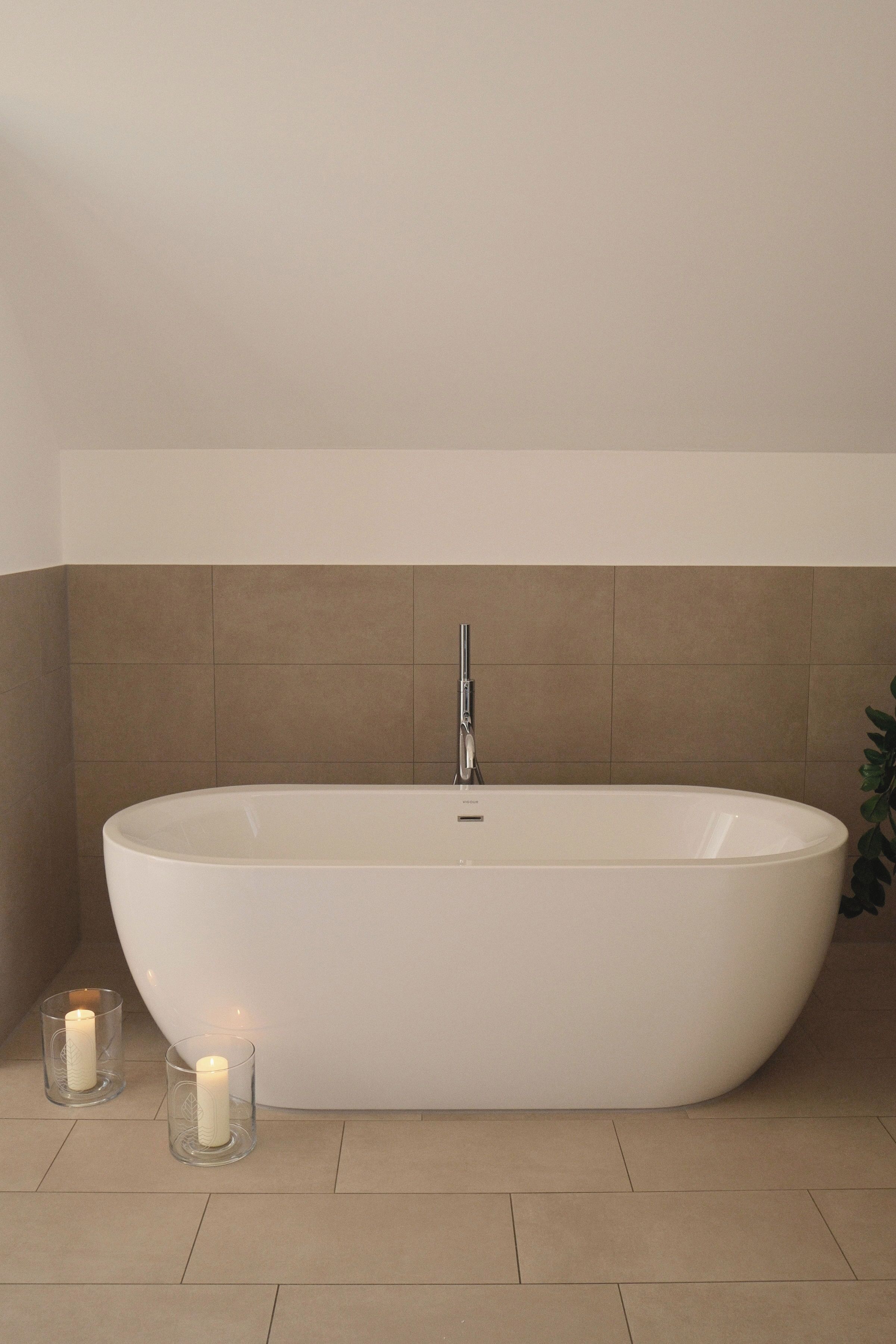 Un baño moderno con una bañera independiente, una vela y una planta en maceta.