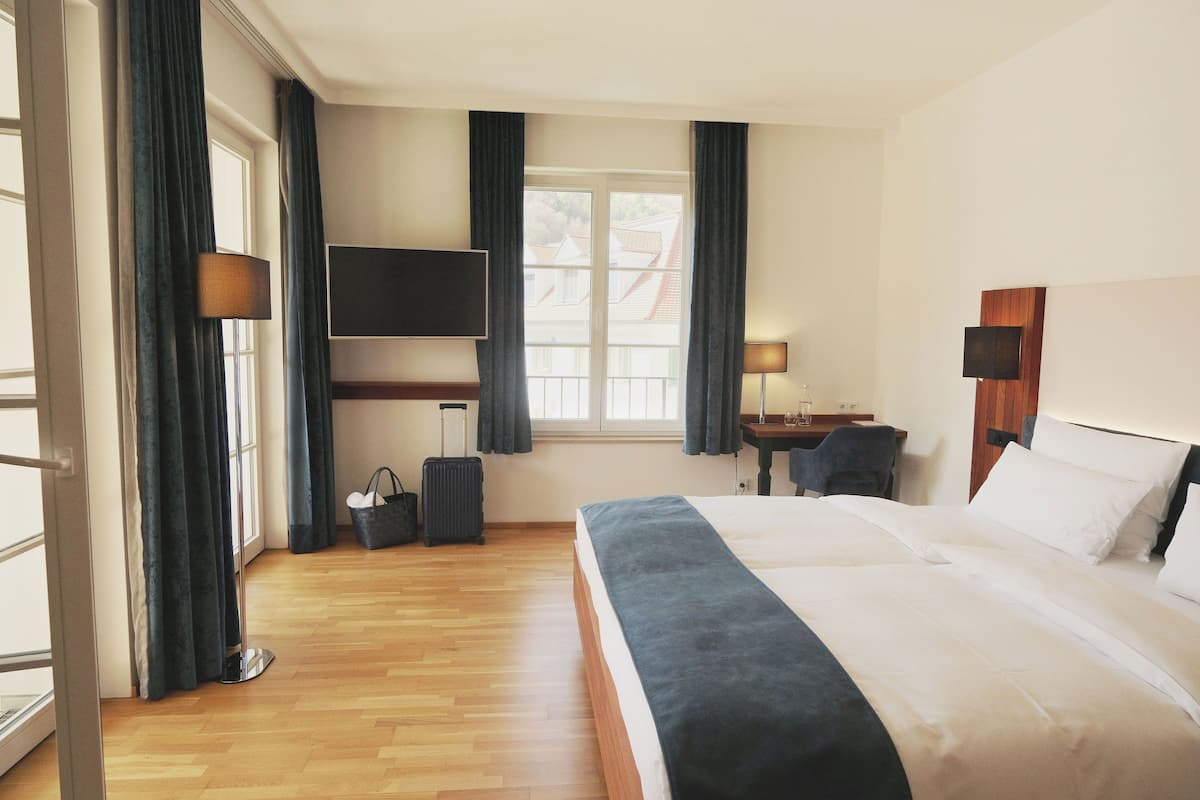 A hotel room with a bed, a desk, a chair, a TV, and a window with curtains.
