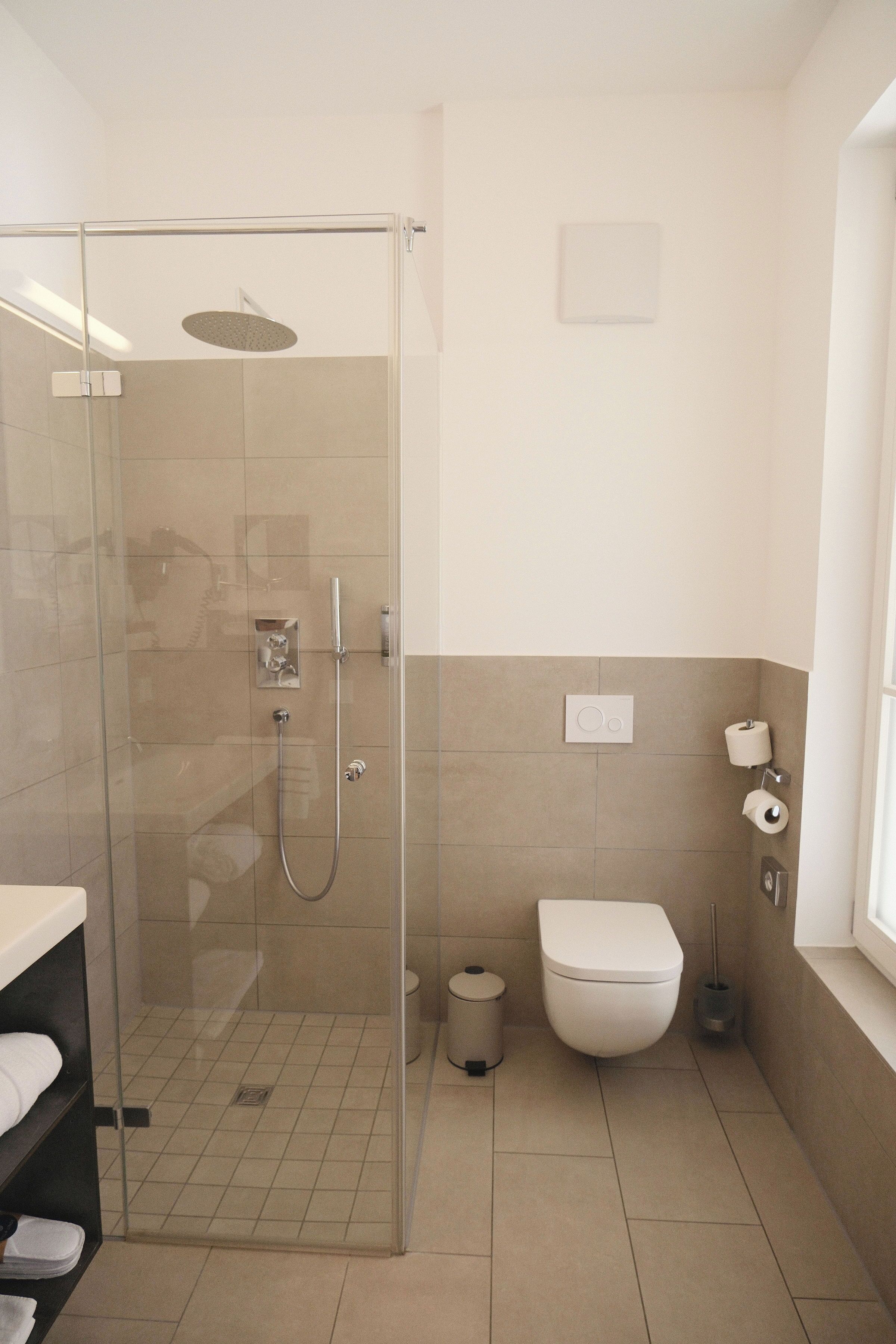 Une salle de bain moderne avec une douche à parois de verre, des toilettes et une poubelle.