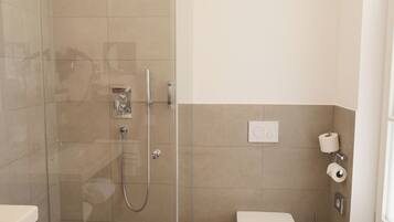Une salle de bain moderne avec une douche à parois de verre, des toilettes et une poubelle.