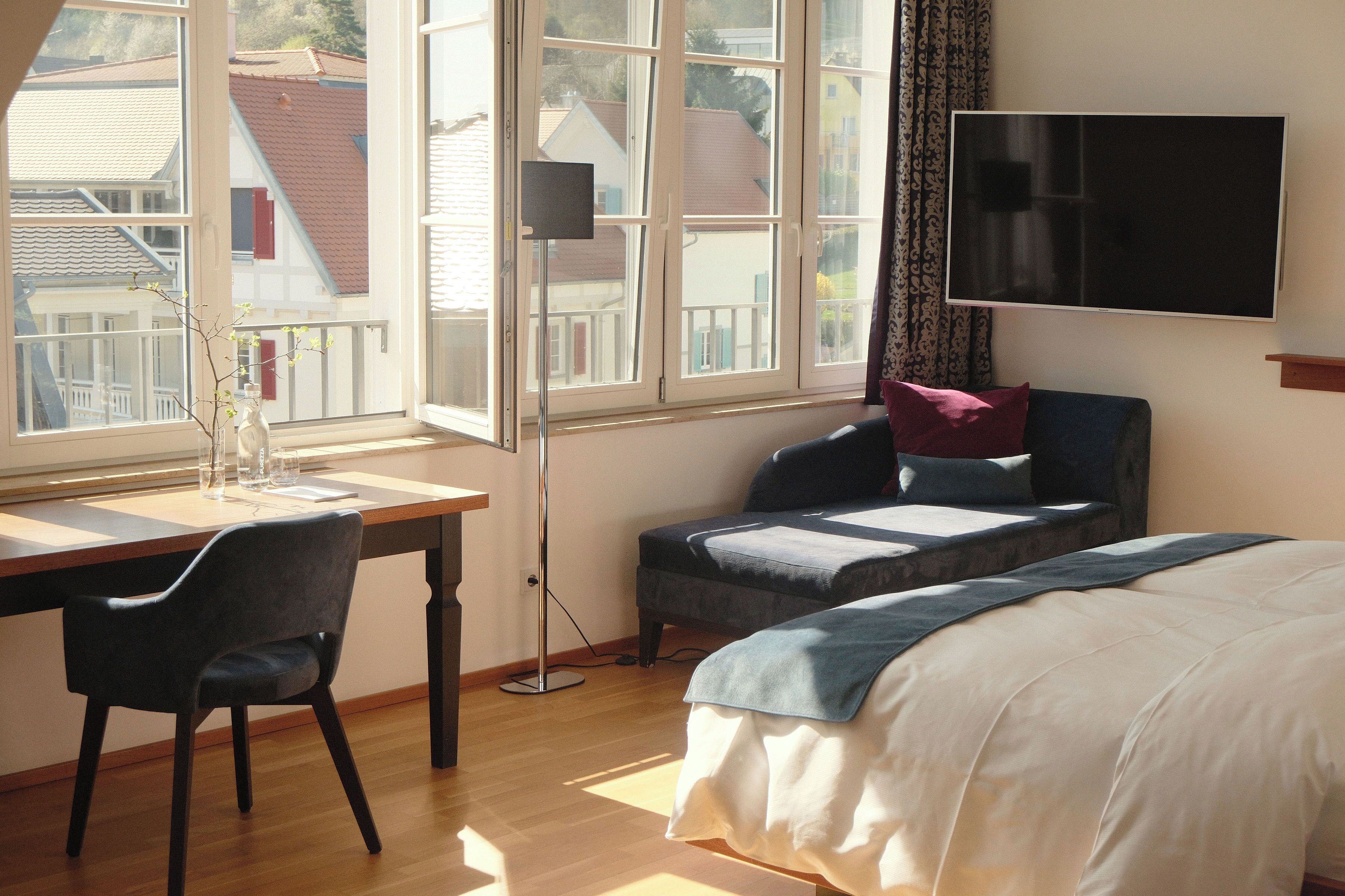 Ein Schlafzimmer mit einem Bett, einem Schreibtisch mit Stuhl, einem Fernseher und einem Fenster mit Blick auf Gebäude.