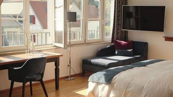 Ein Schlafzimmer mit einem Bett, einem Schreibtisch mit Stuhl, einem Fernseher und einem Fenster mit Blick auf Gebäude.
