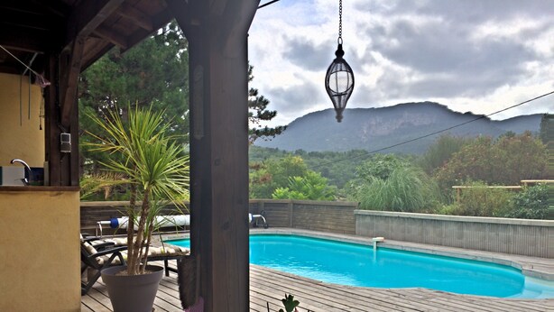 Une piscine avec une terrasse en bois, entourée de plantes en pot et offrant une vue sur les montagnes.