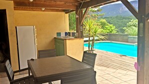 Un espace extérieur abrité comprenant une piscine, une table, des chaises, un réfrigérateur et un petit coin cuisine.