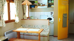 Une cuisine compacte avec un coin repas comprenant un banc et une table, un four à micro-ondes et une petite fenêtre avec des rideaux.