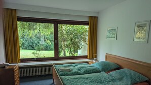 A bedroom with two beds, a window with curtains, a radiator, and a dresser. - Charming 70s house with large garden (Heide)