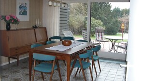 A dining area with a wooden table and blue chairs, a cabinet, and a view of the outdoors through a glass door. - Charming 70s house with large garden (Heide)