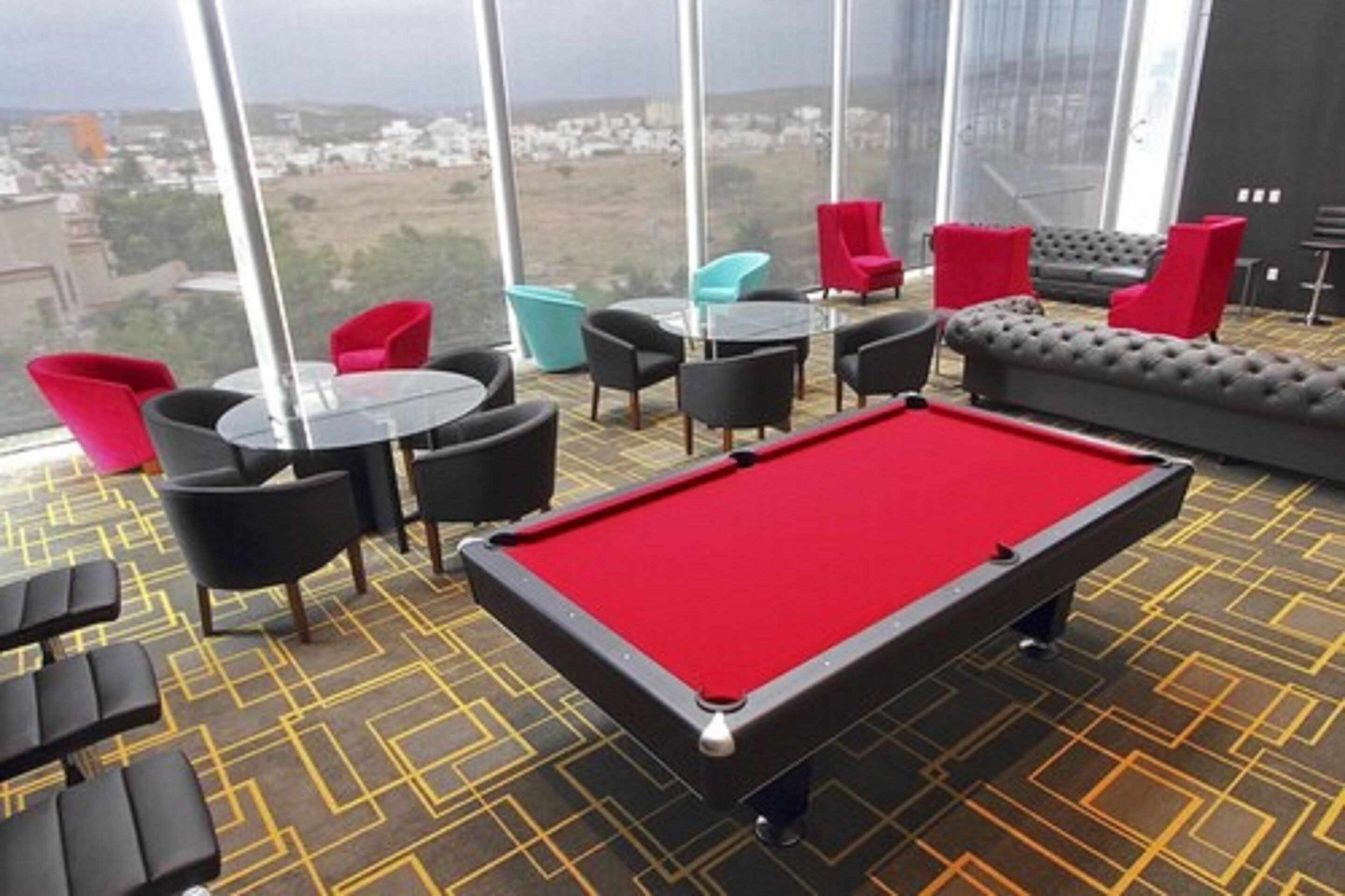 A pool table with red felt, surrounded by black and red chairs, and a sofa with red cushions.