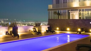 A modern building with a rooftop pool area, including lounge chairs and a water feature.