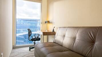 Habitación de hotel moderna con sofá de cuero, escritorio y silla. Un amplio ventanal ofrece vistas a un paisaje urbano.