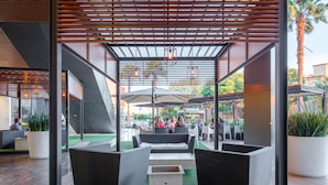 An outdoor seating area with wicker furniture and umbrellas, surrounded by glass walls and a wooden ceiling.