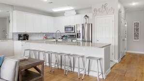 A modern kitchen with white cabinetry, stainless steel appliances, and a central island with bar stools. - Directly Across from Gulf with Views from Every Balcony! The Easiest Access! (Navarre)