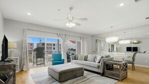 A spacious living room with a large window, a ceiling fan, a sofa, an ottoman, and a small table. - Directly Across from Gulf with Views from Every Balcony! The Easiest Access! (Navarre)