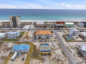 A coastal area with a beach, a road, and several buildings including a multi-story hotel, a blue house with a pool, and a building with a red roof. - Directly Across from Gulf with Views from Every Balcony! The Easiest Access! (Navarre)