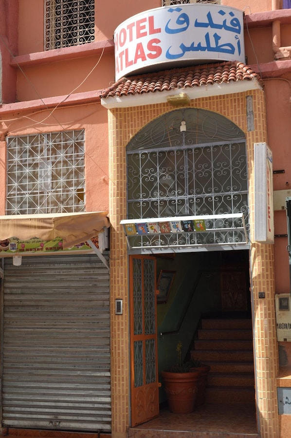 A hotel entrance with a sign in multiple languages, a metal gate, and a staircase leading inside.
