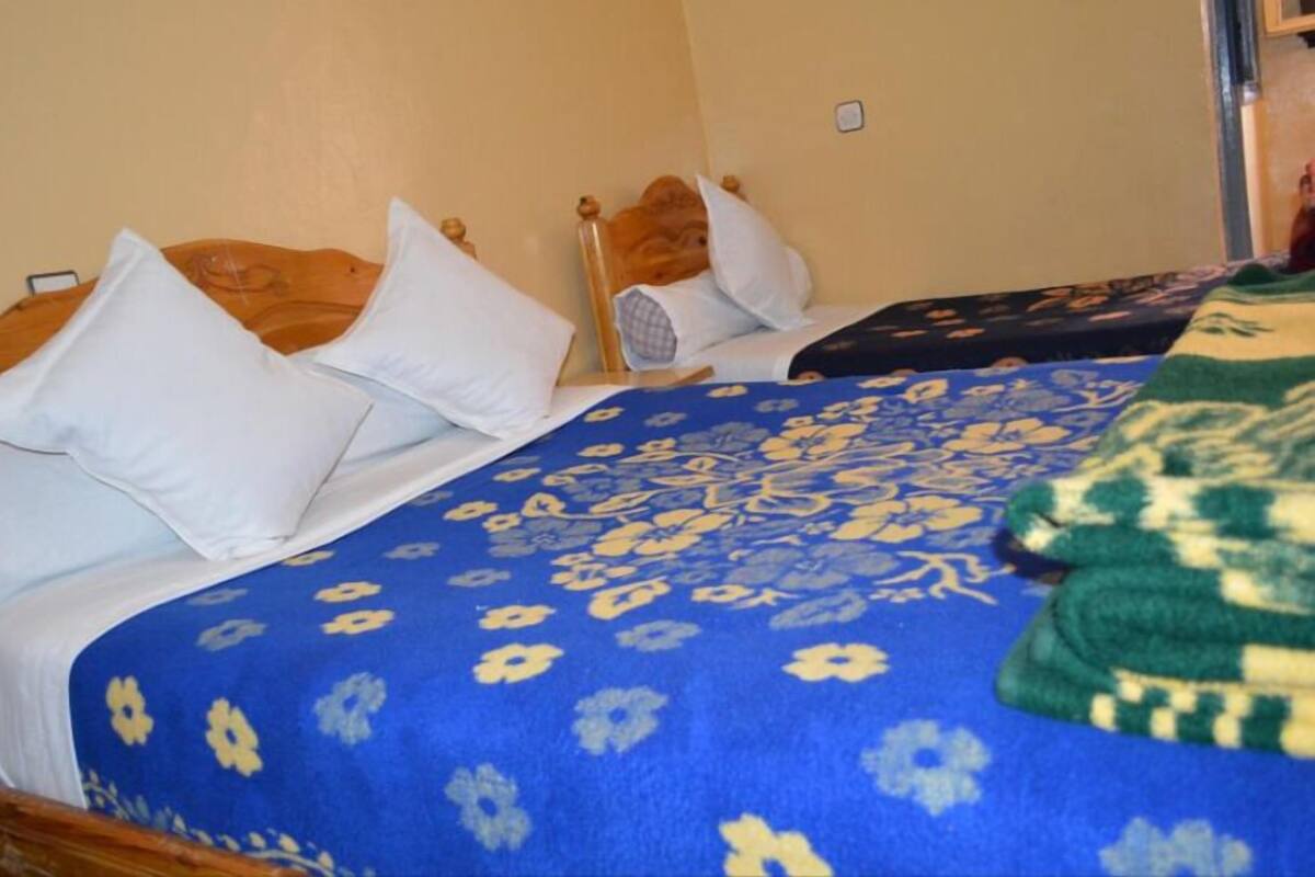 Une chambre d’hôtel avec deux lits, chacun doté d’une tête de lit en bois et d’oreillers blancs. Les lits sont recouverts de couvre-lits à motifs floraux bleus.