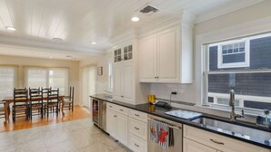 A modern kitchen with white cabinetry, a black countertop, and a dining area with wooden chairs. - Deauville Beach Ocean-side Property (Mantoloking)