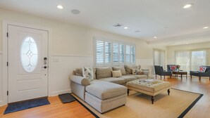 A spacious living room with a sectional sofa, ottoman, and a dining area with two chairs. - Deauville Beach Ocean-side Property (Mantoloking)