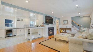 A spacious living area with a fireplace, a sofa, and a kitchen with white cabinets. - Deauville Beach Ocean-side Property (Mantoloking)