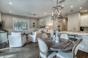 A spacious living room with a dining area, large windows, and a modern kitchen with white cabinets.