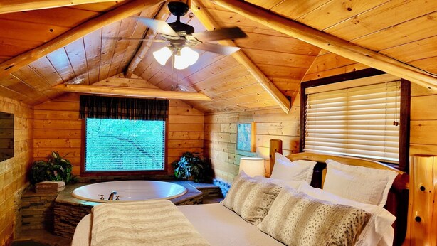 Ein gemütliches Schlafzimmer in einer Hütte mit einem großen Bett, einem Deckenventilator, einem Fenster mit Jalousien und einer Badewanne.